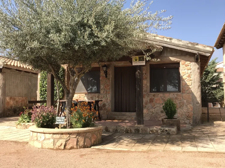 Entrada de una cabaña de El Acuífero, con el muro de mampostería, el olivo y el arriate de flores