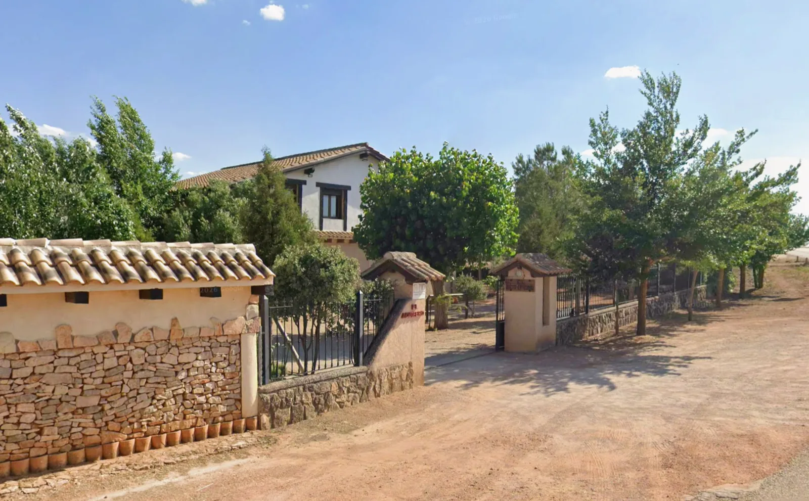 Entrada a la finca de Cabañas El Acuífero, con el muro de piedra y la cancela bajo los árboles