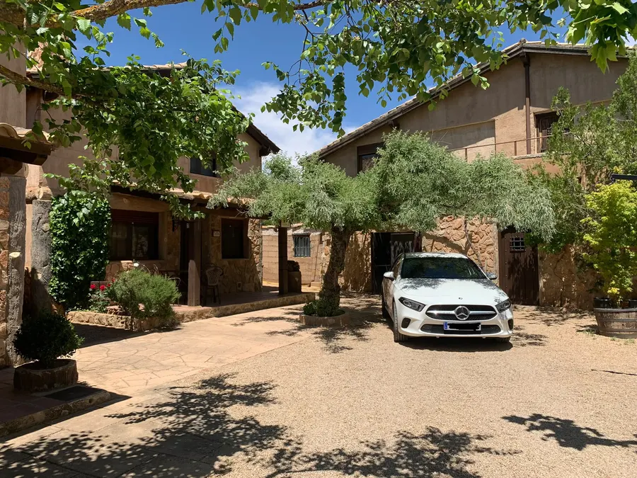 Coche aparcado dentro de la finca de El Acuífero, junto a dos cabañas de piedra de dos alturas y bajo los olivos