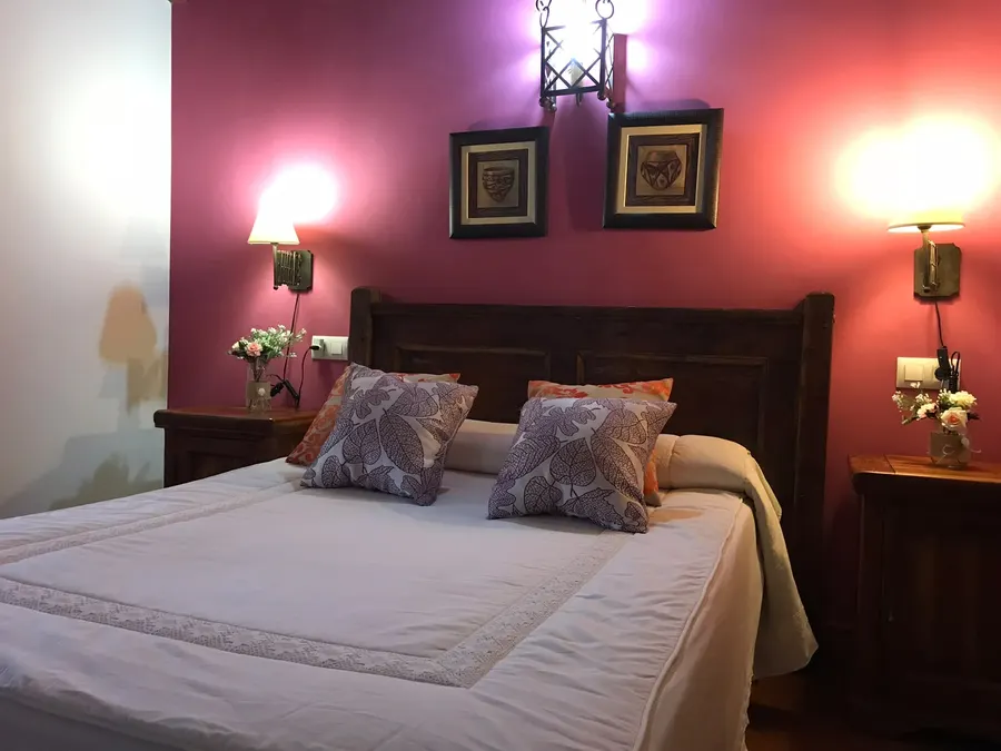 Dormitorio de matrimonio en la buhardilla de una cabaña de El Acuífero, con mesillas de madera, flores y lámparas de pared