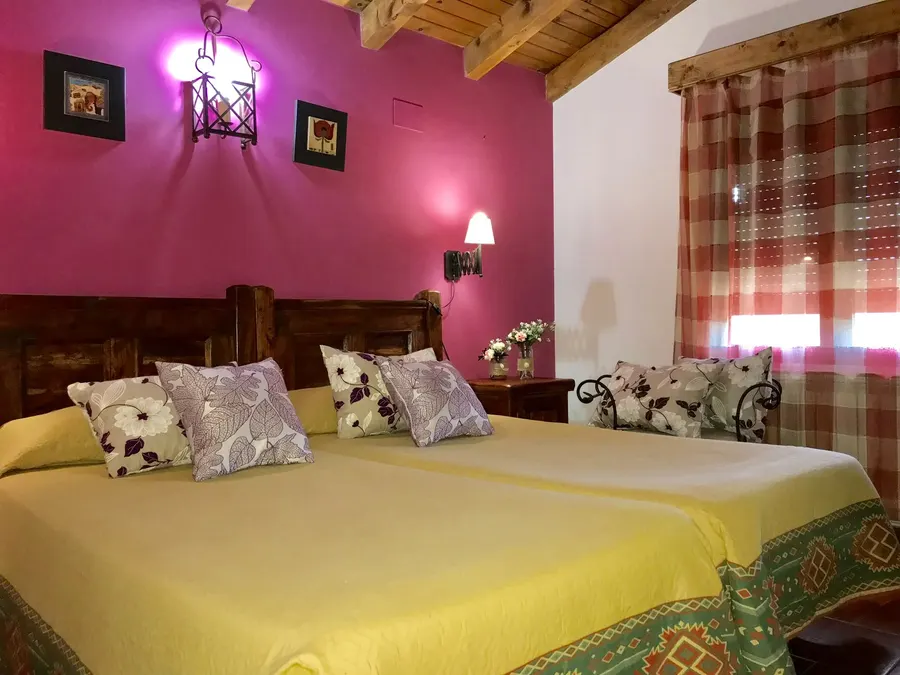 Segundo dormitorio de una cabaña con dos camas individuales juntas, vigas de madera en el techo y cortinas de cuadros