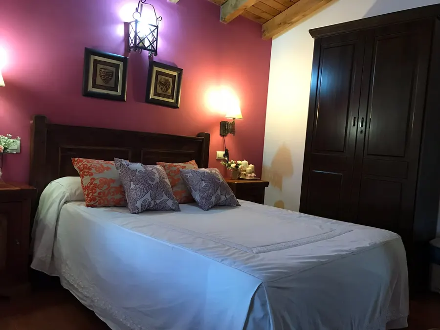 Dormitorio de matrimonio de una cabaña con cabecero de madera maciza, armario, apliques de forja y pared granate