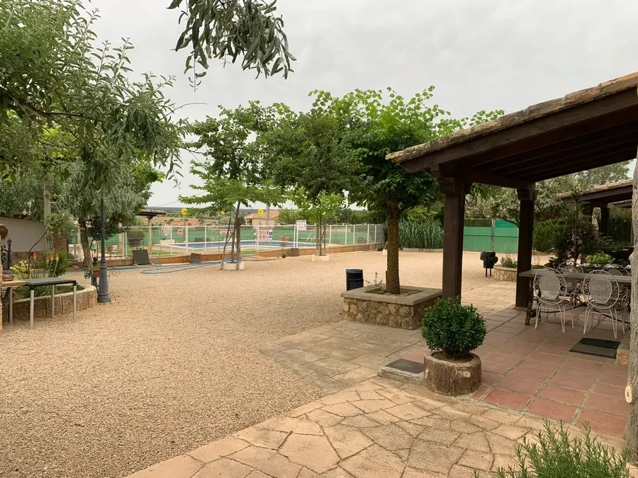 Patio central de El Acuífero con árboles, pérgola de madera con mesa y sillas, y la piscina vallada al fondo