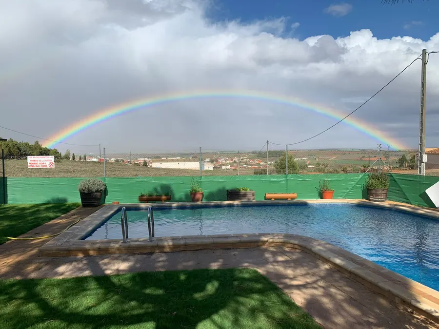 Arcoíris completo sobre la piscina de El Acuífero después de una tormenta, con Ossa de Montiel al fondo