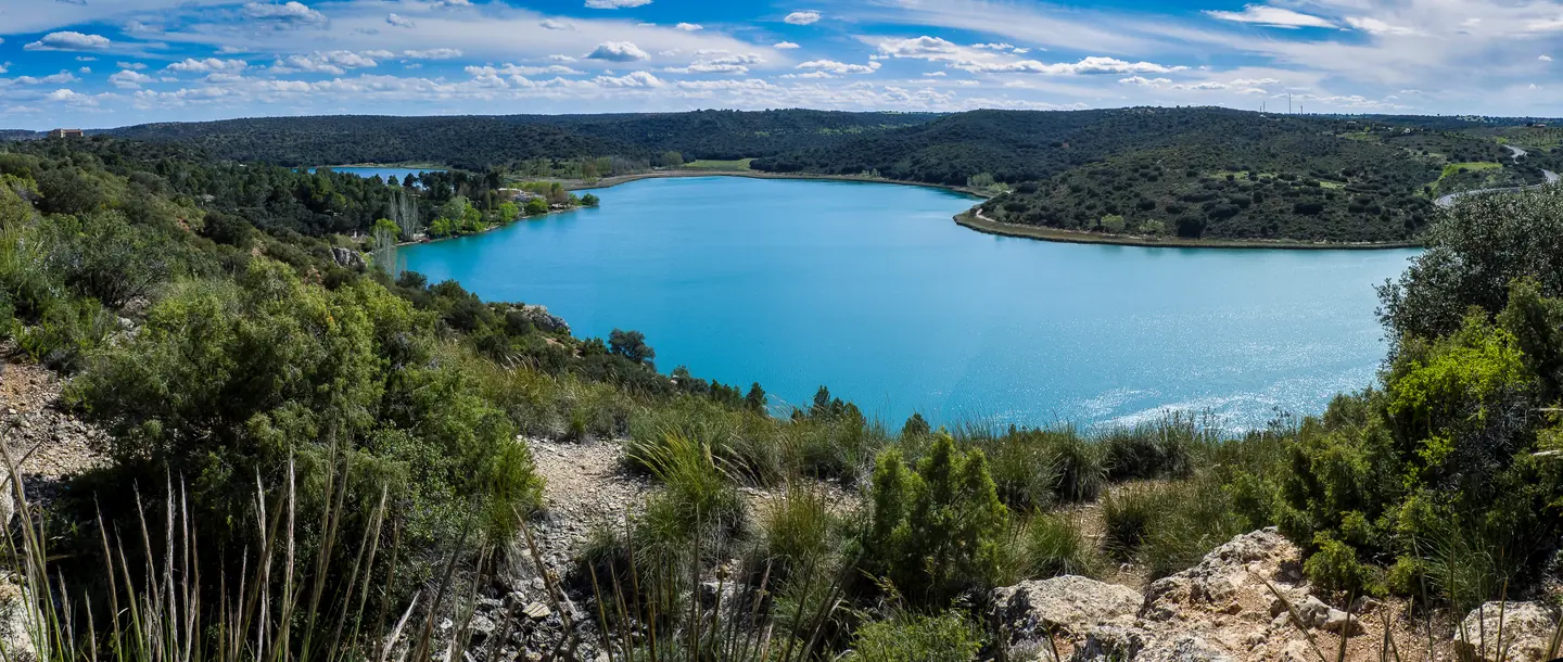 Panorámica de una laguna de Ruidera en un día despejado, con el agua turquesa rodeada de monte bajo y el matorral del primer término